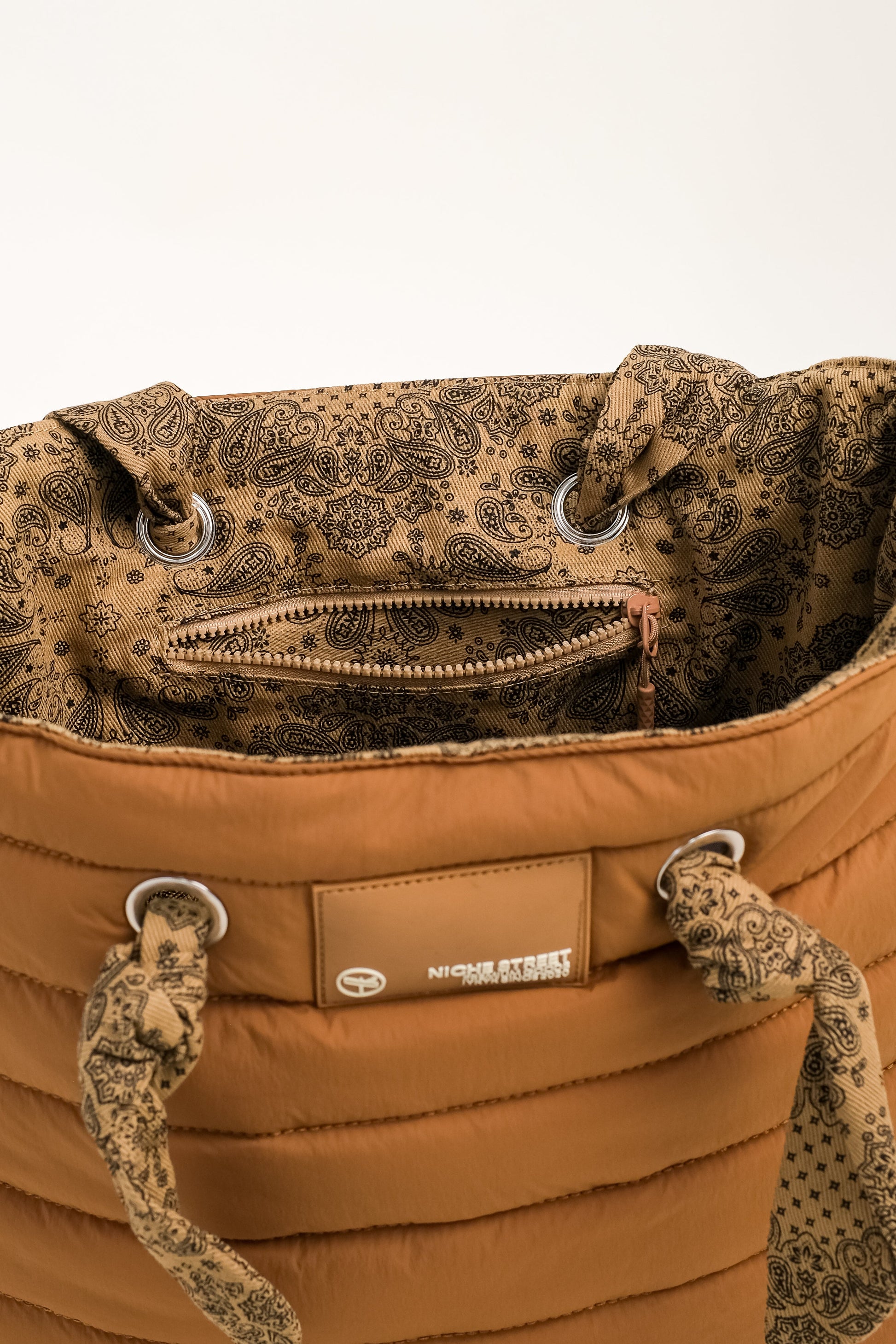 Brown quilted bag with patterned interior and visible brand logo on a white background